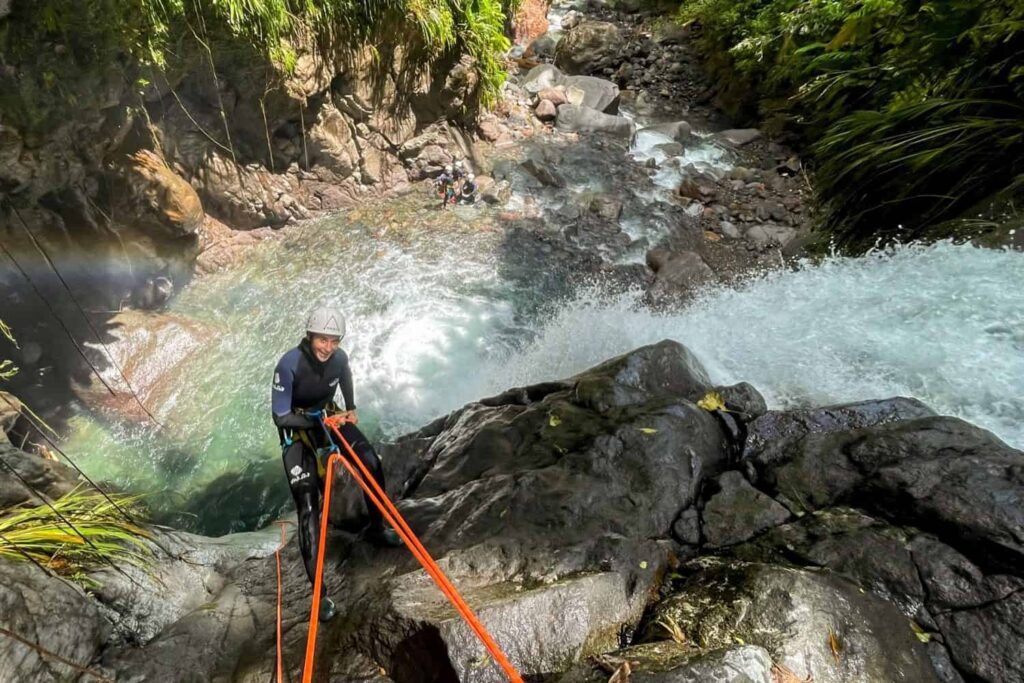 Canyoniste en rappel au-dessus d'une vasque, arc-en-ciel dans les embruns, aux cascades de Vauchelet, Rivière Noire (Saint-Claude)