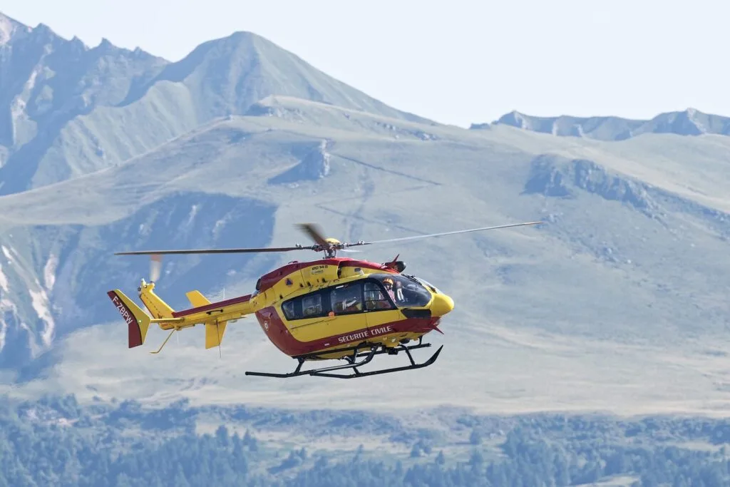 Hélicoptère jaune et rouge Dragon de la Sécurité civile en vol devant un relief de montagne